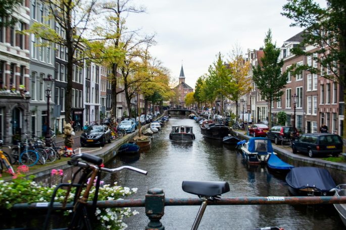 A canal lined with historic buildings and boats, framed by autumn foliage.