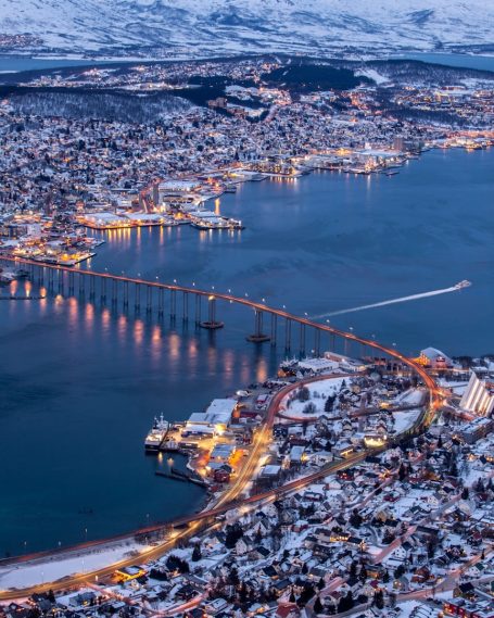 Snow-covered town with lights reflecting on a bay and a bridge crossing the water.